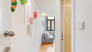 Un couloir avec un plancher en bois, un canapé gris et une fenêtre donnant sur des immeubles.