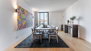 A modern dining area with a long table, chairs, and a large abstract painting on the wall.