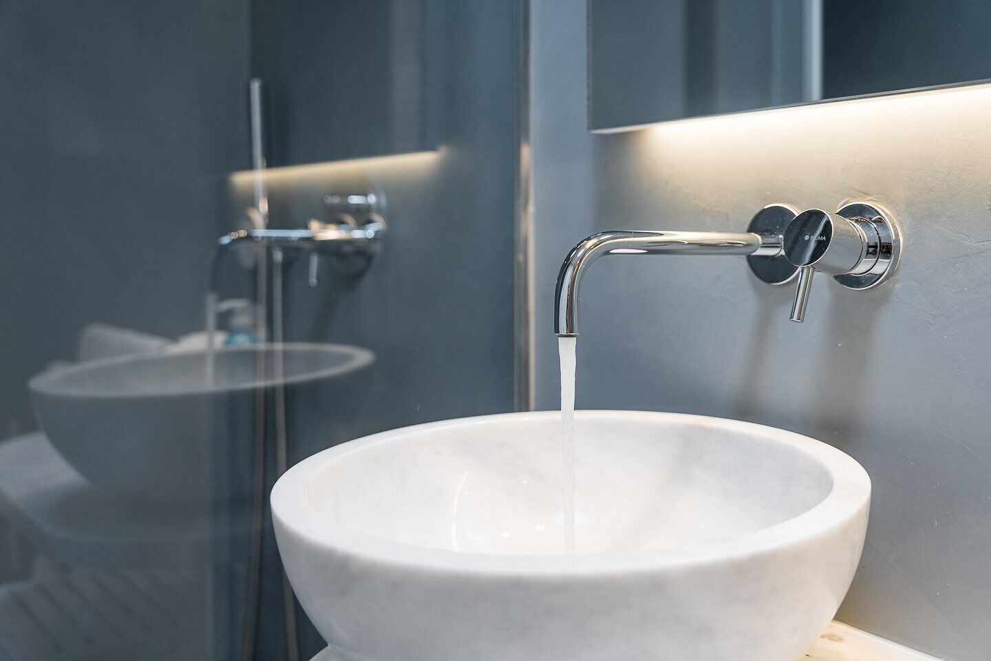 A modern bathroom with a white ceramic sink, a chrome faucet, and a mirror reflecting the sink and faucet.