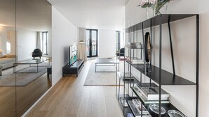 A modern living room with a glass partition, a black bookshelf, and a view of the city through large windows.