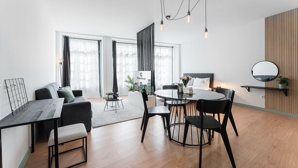 Et moderne hotelværelse med spiseplads, en seng med udsigt over bybilledet og et spejl med sort ramme på væggen.