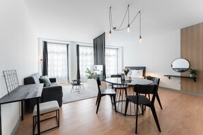 A modern hotel room with a dining area, a bed with a cityscape view, and a black-framed mirror on the wall.