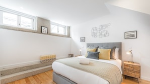 Een slaapkamer met een bed, nachtkastjes, een raam en een kunstwerk aan de muur.
