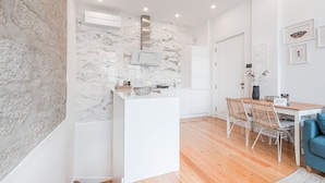 Een moderne keuken met een marmeren spatwand, witte kasten en een eethoek met houten vloer en rieten stoelen.