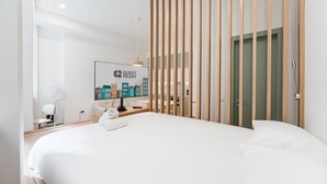 A hotel room with a bed, a desk with a computer, a chair, a wall-mounted TV displaying 'GUEST READY', and a wooden partition. - GuestReady - A modern stay in Downtown (Porto)