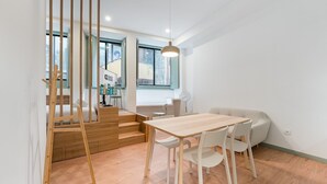 A modern hotel room with a wooden staircase, a dining area with a wooden table and white chairs, and a large window providing a view of the outside. - GuestReady - A modern stay in Downtown (Porto)