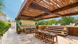 Una terrazza esterna con una pergola in legno, un murale, un'area pranzo con sedie e tavolo, e una scala che conduce a un livello superiore.
