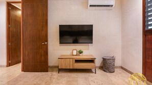 Una stanza con una porta in legno, una TV a parete, un armadietto in legno e un cestino.