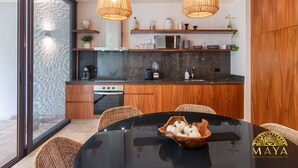 Una cucina moderna con mobili in legno, un piano di lavoro nero e sedie in vimini. Ci sono due lampade a sospensione in vimini, un forno a microonde e una macchina per il caffè sul bancone.