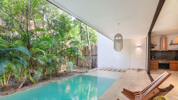 Area piscina moderna con solarium in legno e poltrone relax, immersa nel verde e delimitata da una staccionata in bambù.