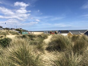 Uma praia com dunas e cabanas de praia ao primeiro plano.