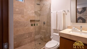 A modern bathroom with a glass-enclosed shower, a toilet, and a vanity with a sink and mirror. - NHOA 108B Lux 1BR Condo Plunge Pool in Aldea Zama (Tulum)