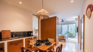 A modern kitchen with wooden cabinets, a dining table set for four, and a large window overlooking a balcony. - NHOA 108B Lux 1BR Condo Plunge Pool in Aldea Zama (Tulum)