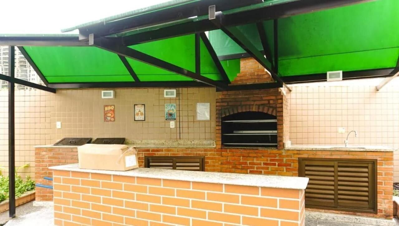 An outdoor kitchen with a brick counter, two pizza ovens, and a green awning.