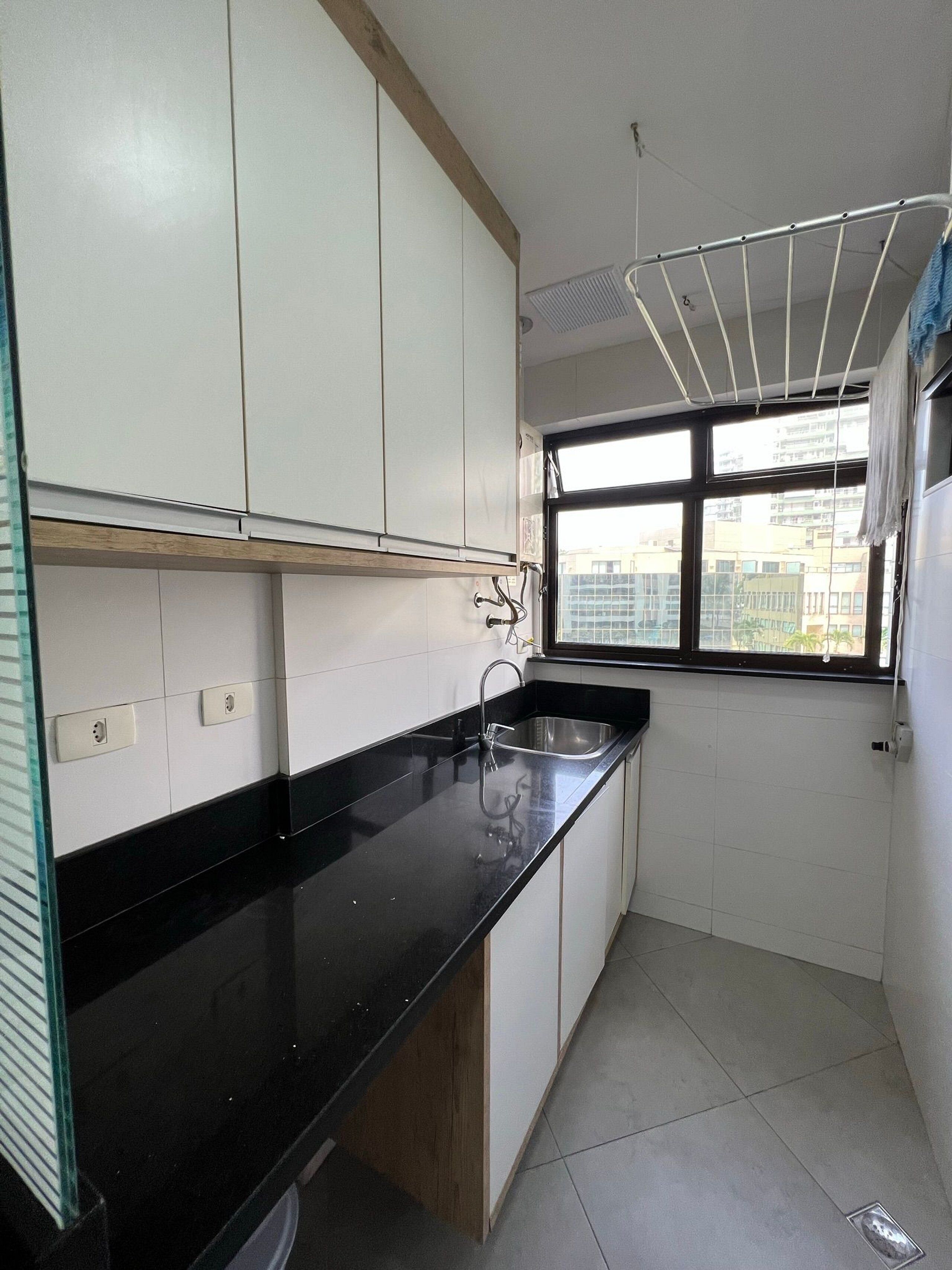 A kitchen with white cabinets, a black countertop, a stainless steel sink, and a window with a view of buildings.