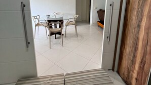 An open doorway leading to a dining area with a table and chairs, a wooden floor, and a view of a hallway. - LIBERTY PLACE - PARQUE DAS ROSAS (Rio de Janeiro)