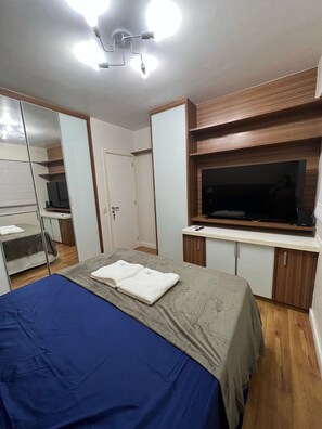 Quarto com cama, televisão, espelho e guarda-roupa.