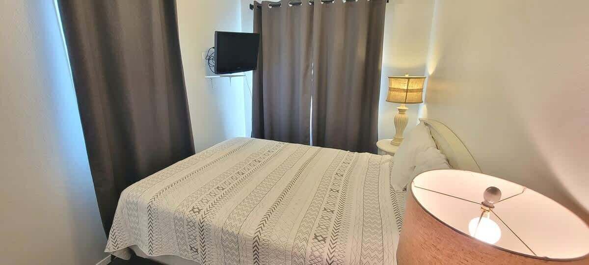 A bedroom with a bed, a bedside lamp, and a TV mounted on the wall.