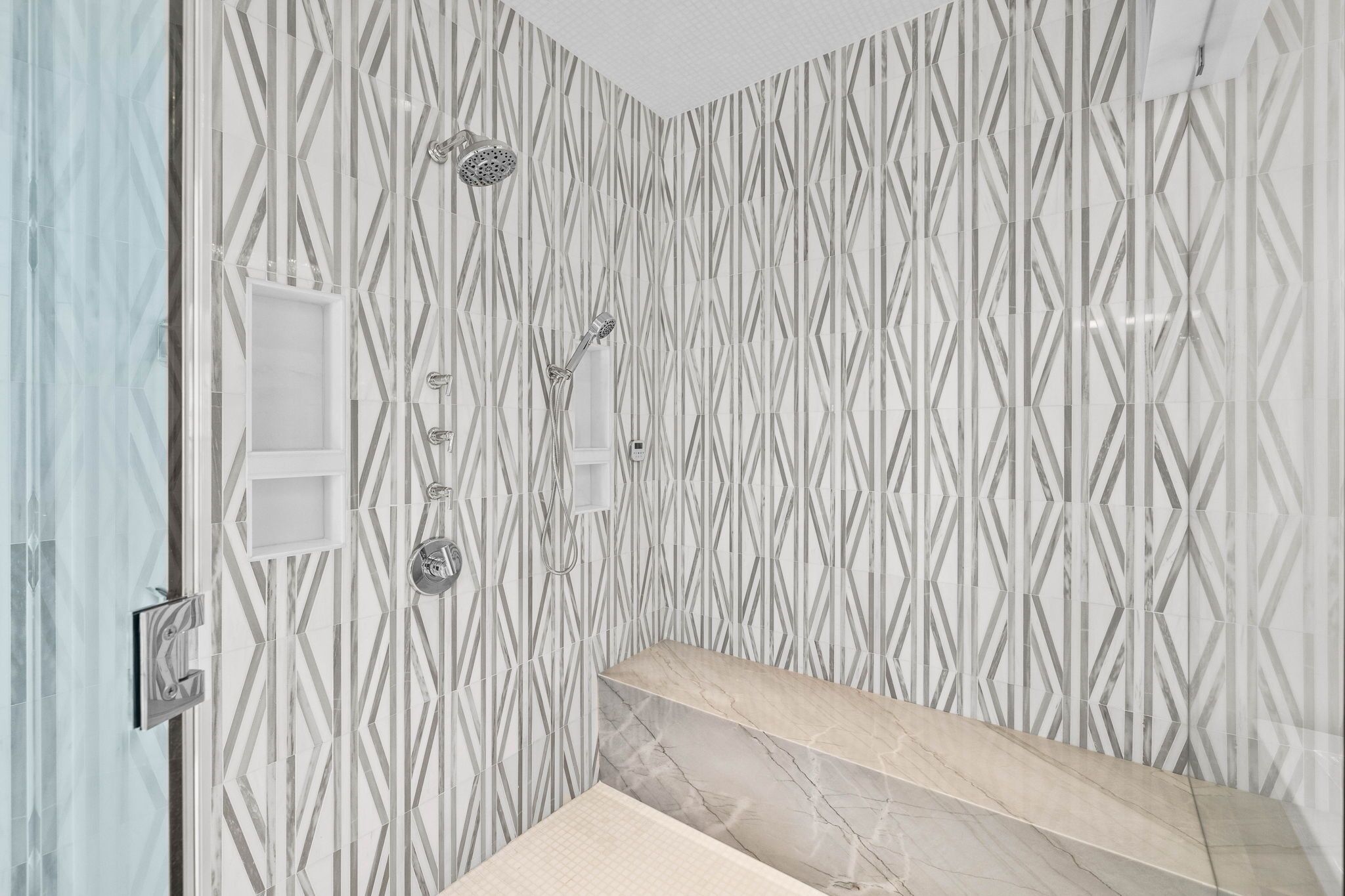 Ein Badezimmer mit Wand in geometrischem Muster, einer Dusche inklusive Handbrause und einem Marmorwaschtisch.