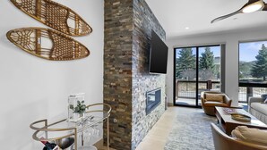 Ein modernes Wohnzimmer mit Kamin aus Stein, großen Fenstern und Blick ins Freie.