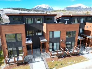 A modern multi-story building with large windows and a flat roof, surrounded by a mountainous landscape. - 541 Center Circle 3br 3.5ba 3 Bedroom Townhouse by RedAwning (Silverthorne)