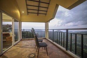 A balcony with a view of the countryside, a chair, and a table with a cushion. - Eagles Wings Abode (Coonoor)