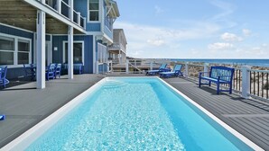 Piscina com cadeiras azuis e um deck, com vista para o oceano.