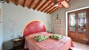 Ein Schlafzimmer mit einem großen Bett, einer Holzbalkendecke, einer Heizung und einer Tür mit Glasfeldern.