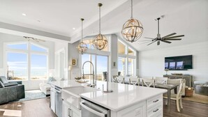 Uma cozinha moderna com uma ilha grande, luminárias pendentes e um ventilador de teto.