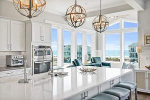 Een moderne keuken met witte kasten, roestvrijstalen apparatuur en een groot eiland. Drie pendellampen met een geometrisch ontwerp.