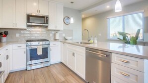 Una cocina moderna con armarios blancos, electrodomésticos de acero inoxidable, lavavajillas y una ventana con persianas.
