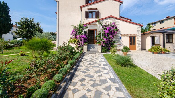 A two-story house with a stone pathway leading to the entrance, surrounded by well-maintained gardens and a clear sky. - Apartments Bungavilia (Rovinj)