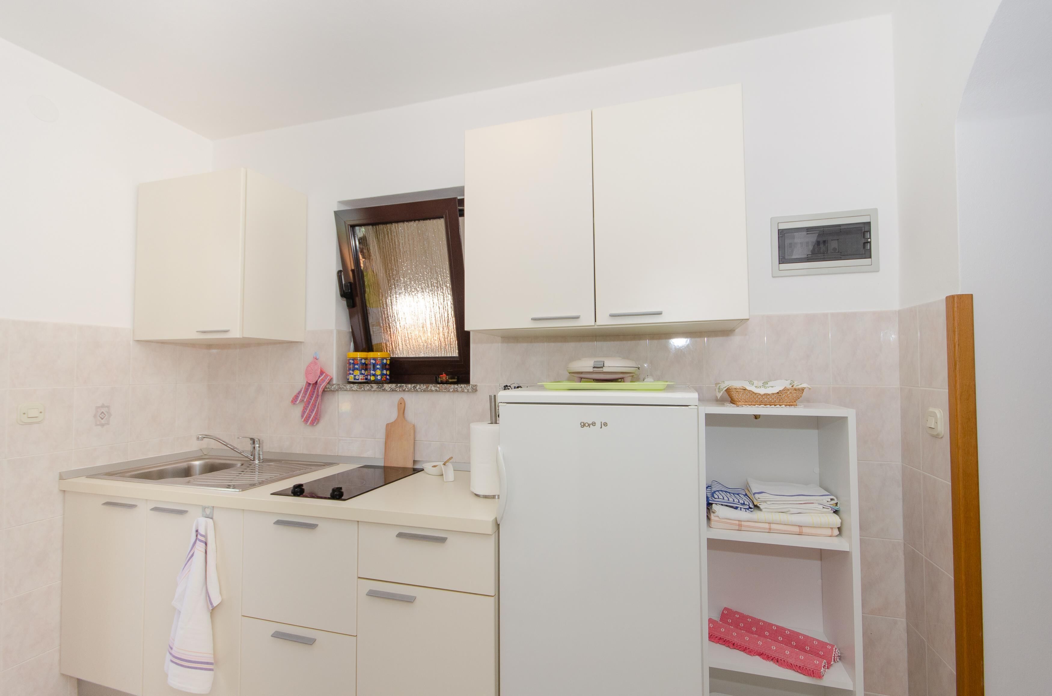 A compact kitchen with a sink, a refrigerator, and a window with a curtain.