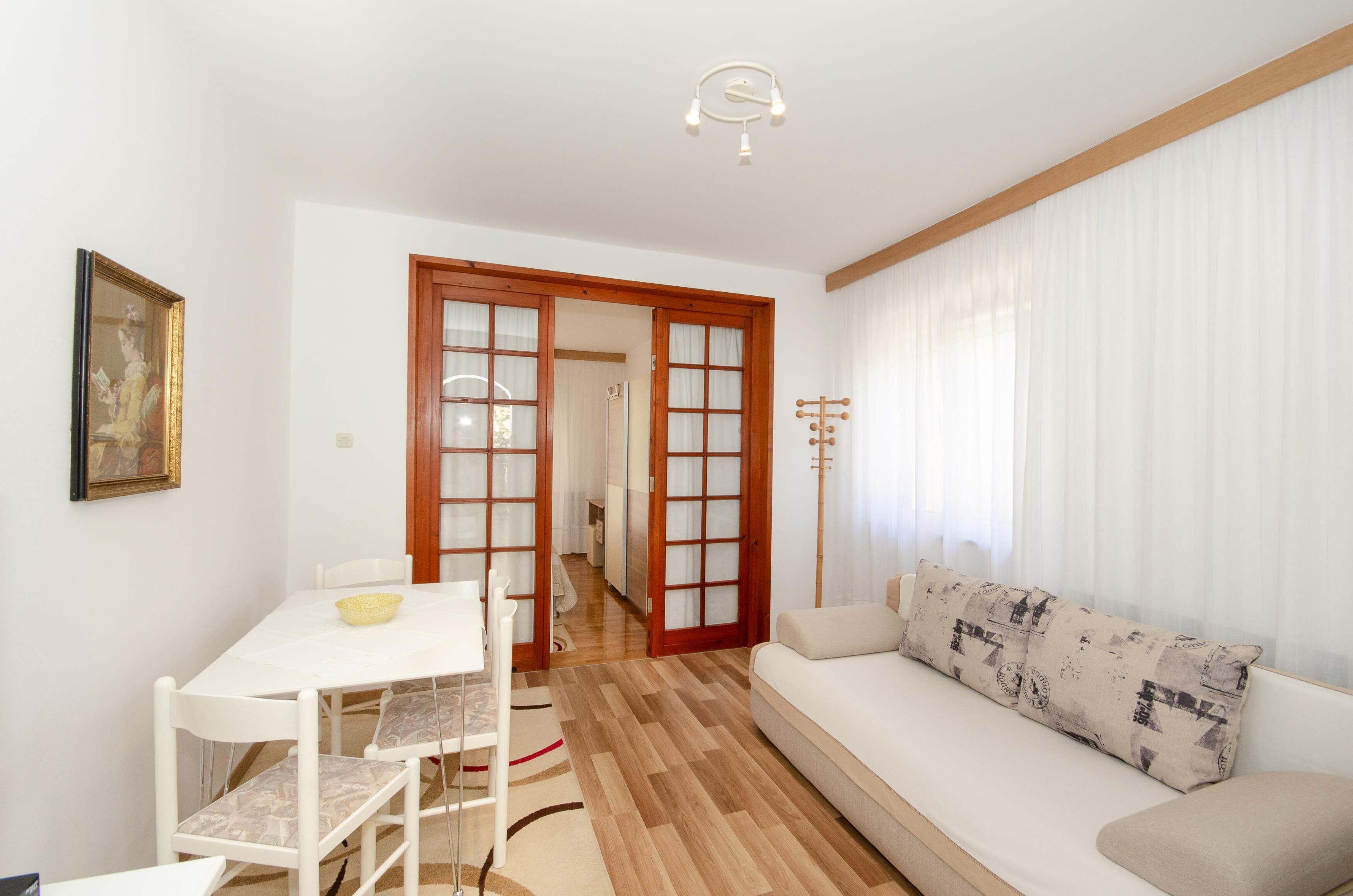 A living room with a white sofa, a dining table with chairs, and a wooden floor.