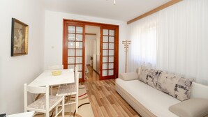A living room with a white sofa, a dining table with chairs, and a wooden floor. - Apartments Bungavilia (Rovinj)