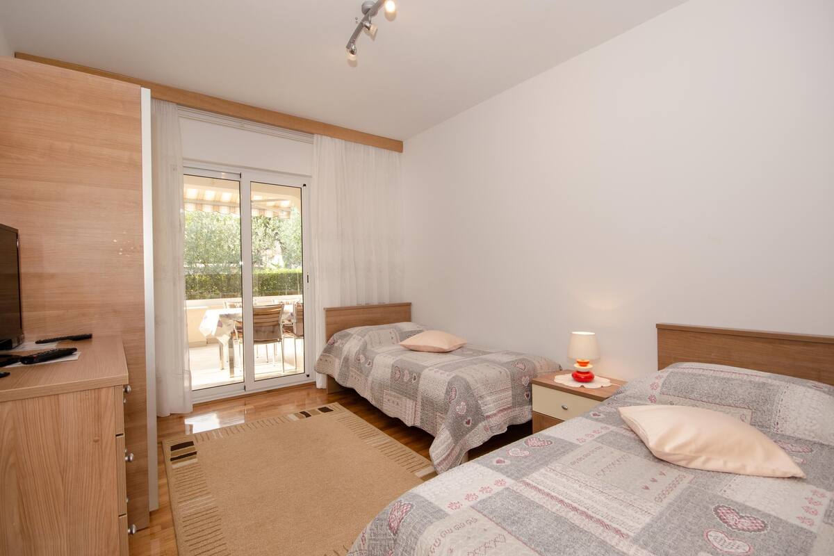 Quarto com duas camas, penteadeira de madeira, escrivaninha com luminária e porta de vidro deslizante para área externa.