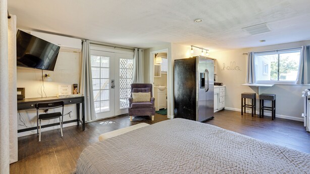 A bedroom with a large bed, a desk with a chair, a television, a refrigerator, and a window with curtains. - 5 Mi to Dtwn: Pet-friendly Phoenix Studio w/ Yard (Phoenix)