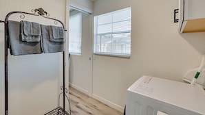 A laundry area with a metal rack holding towels, a washing machine, and a window with blinds. - Modern Tiny Home ~ 5 Mi to Downtown Phoenix! (Phoenix)