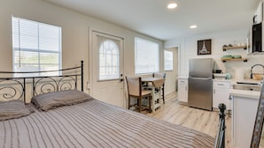 A compact bedroom with a bed, bedside tables, and a desk with a chair. Adjacent is a kitchenette with a refrigerator, stove, and sink. - Modern Tiny Home ~ 5 Mi to Downtown Phoenix! (Phoenix)