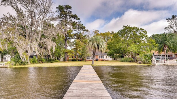 A wooden dock leading to a house surrounded by trees and water. - Jacksonville Vacation Home w/ Trout River Access (Jacksonville)