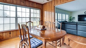A dining area with a wooden table and chairs, a large window, and a living room with a sofa and television. - Jacksonville Vacation Home w/ Trout River Access (Jacksonville)