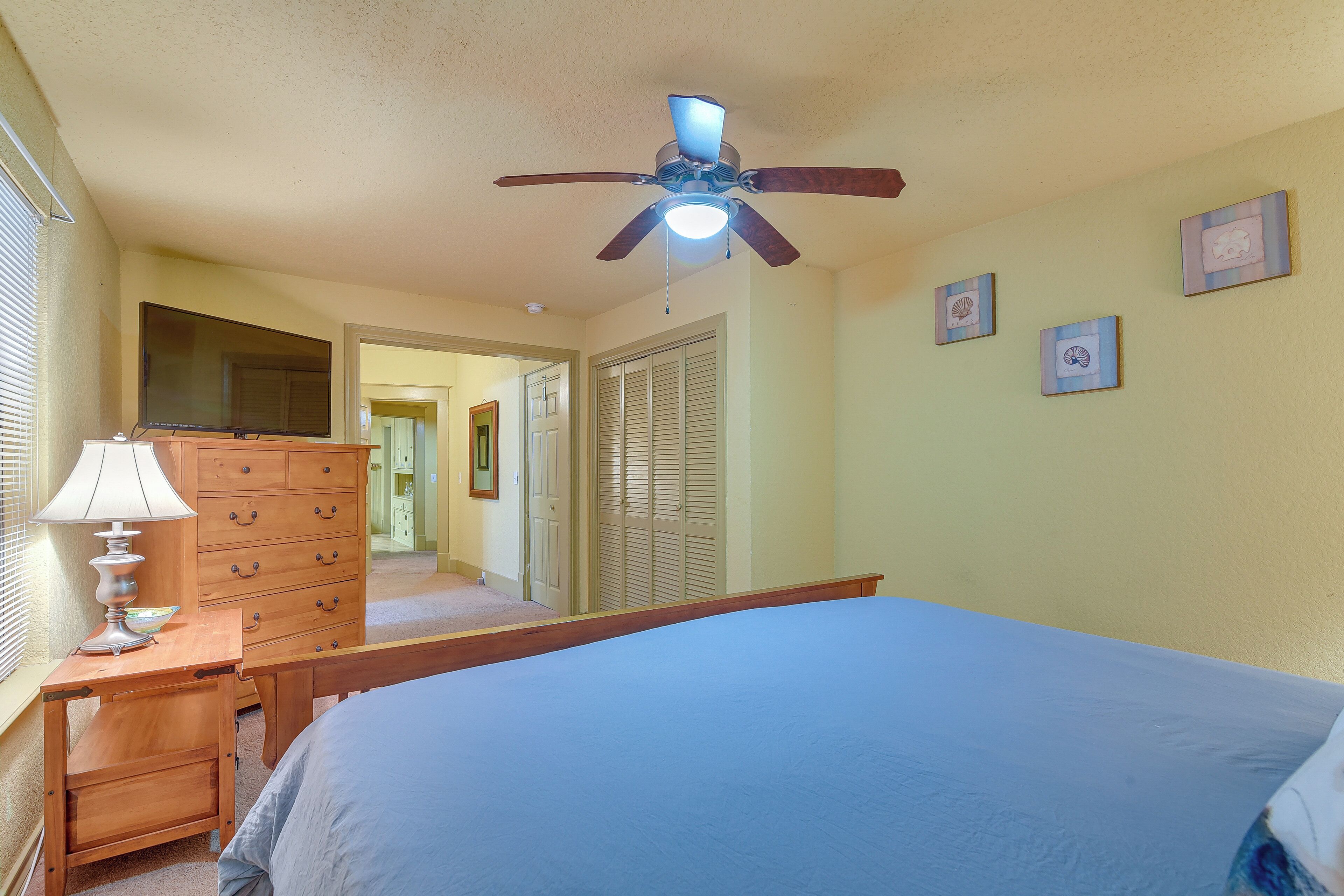A bedroom with a bed, a dresser, a ceiling fan, and framed pictures on the wall.