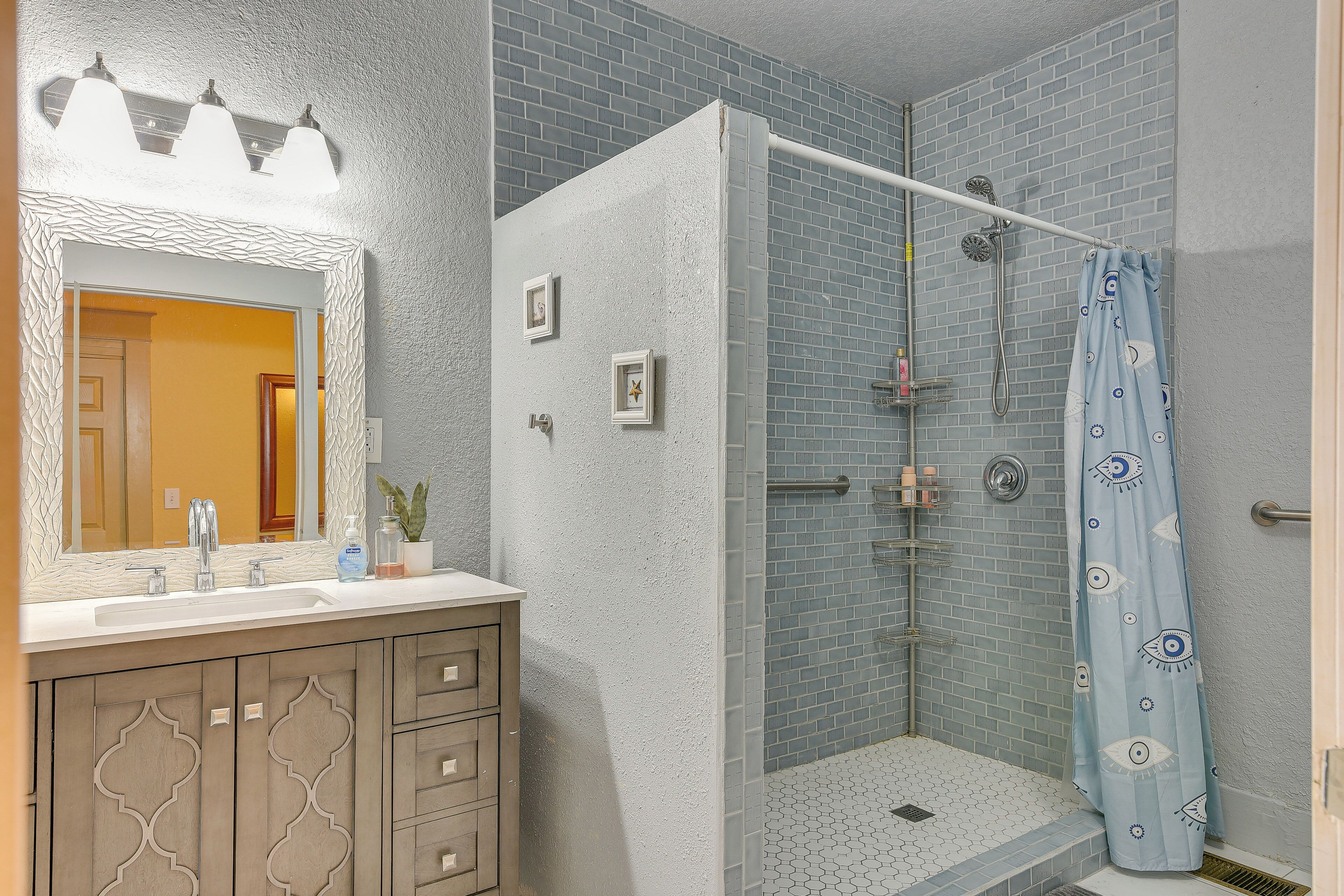 A bathroom with a white vanity, a large mirror, a shower with a glass door, and a blue shower curtain.