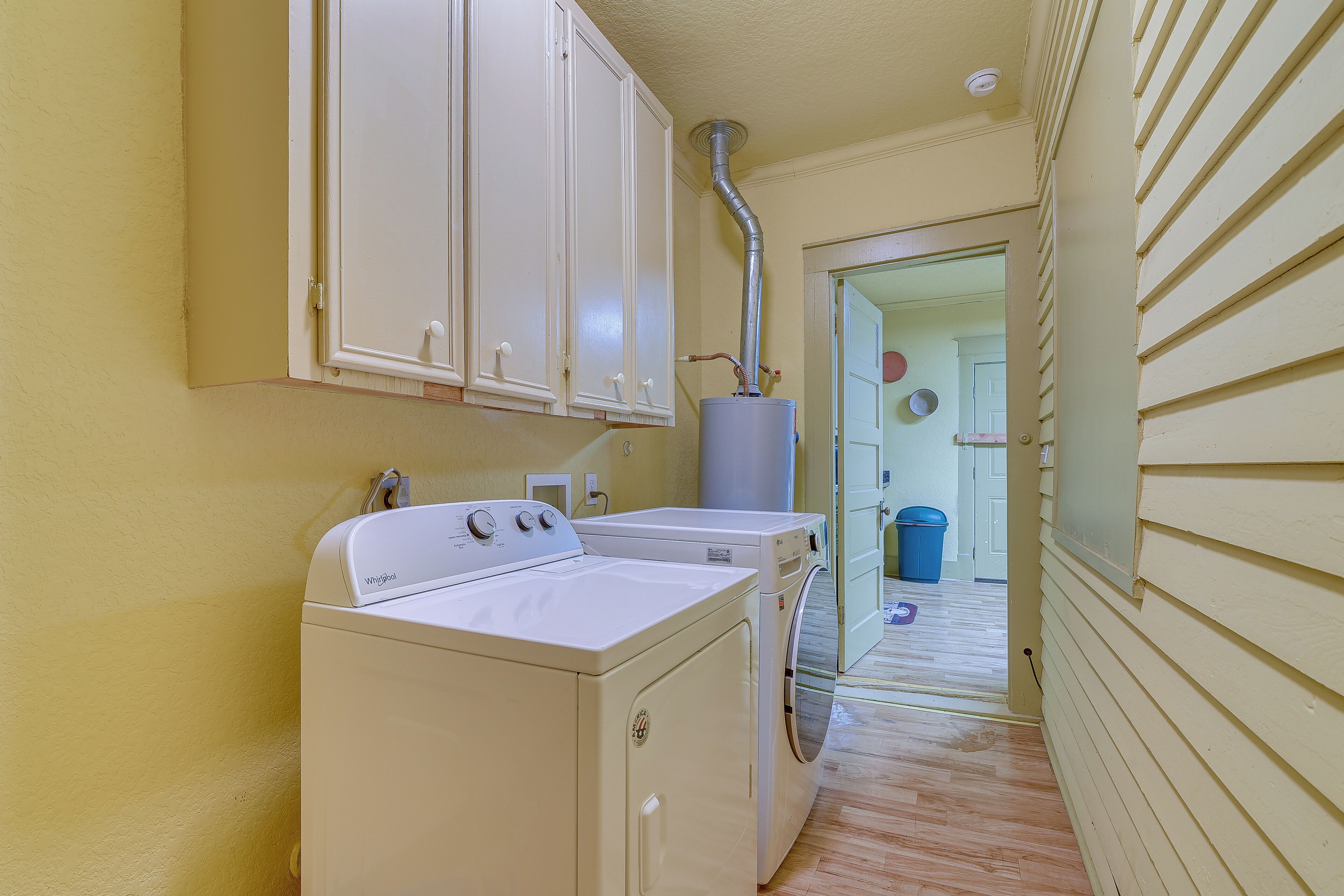 A laundry room with two washers and a dryer, a water heater, and a door leading to another room.