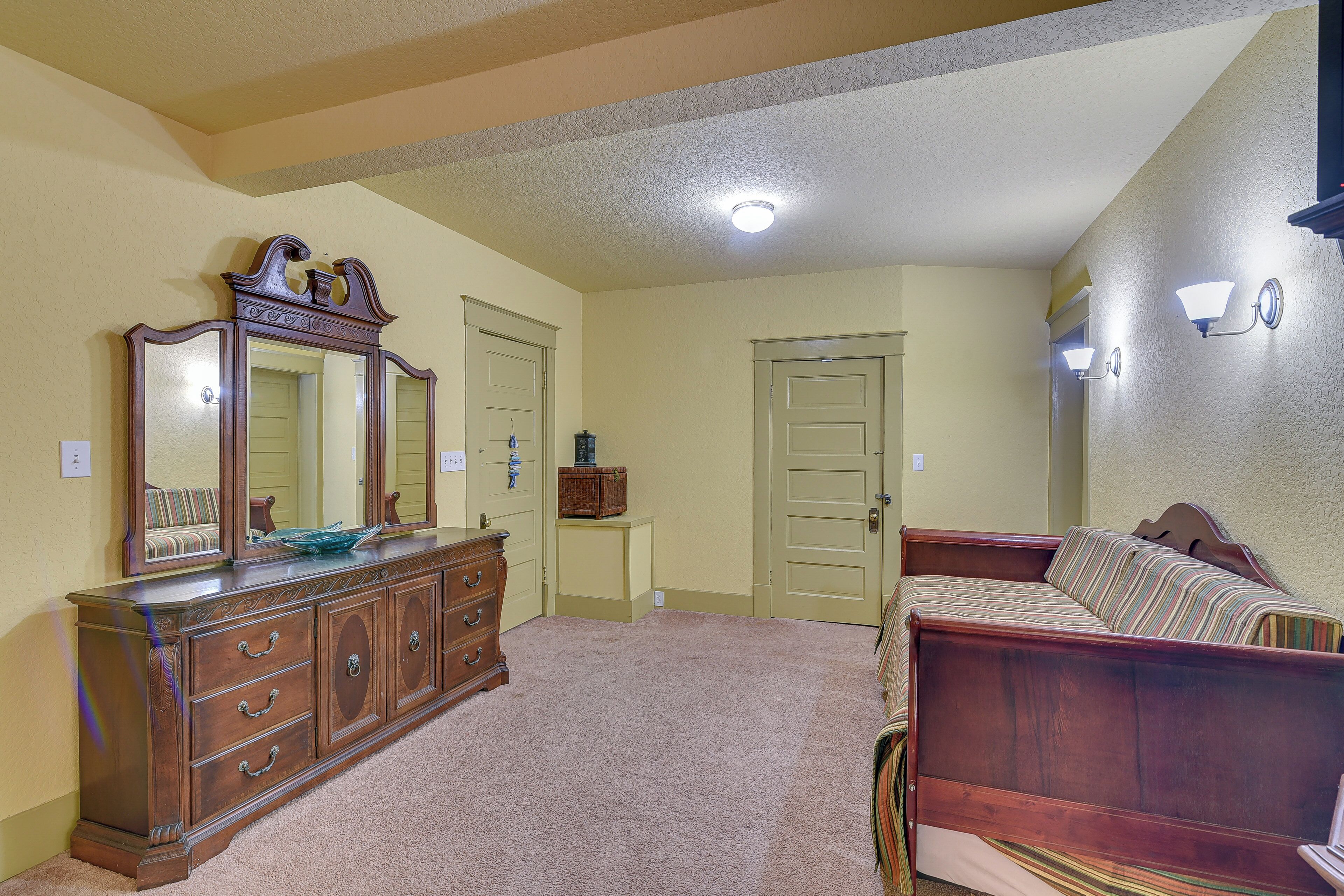 Une chambre à coucher avec une commode en bois, un lit, un miroir et une porte.
