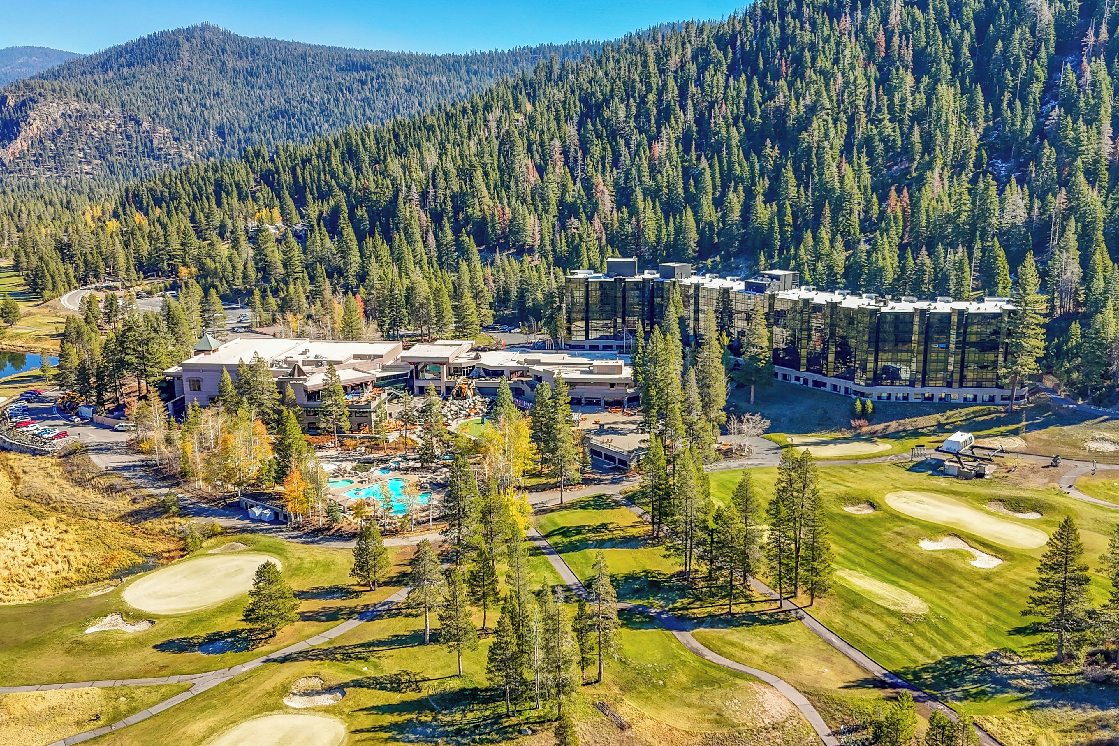 An aerial view of a resort with a golf course, a swimming pool, and a mountainous backdrop.