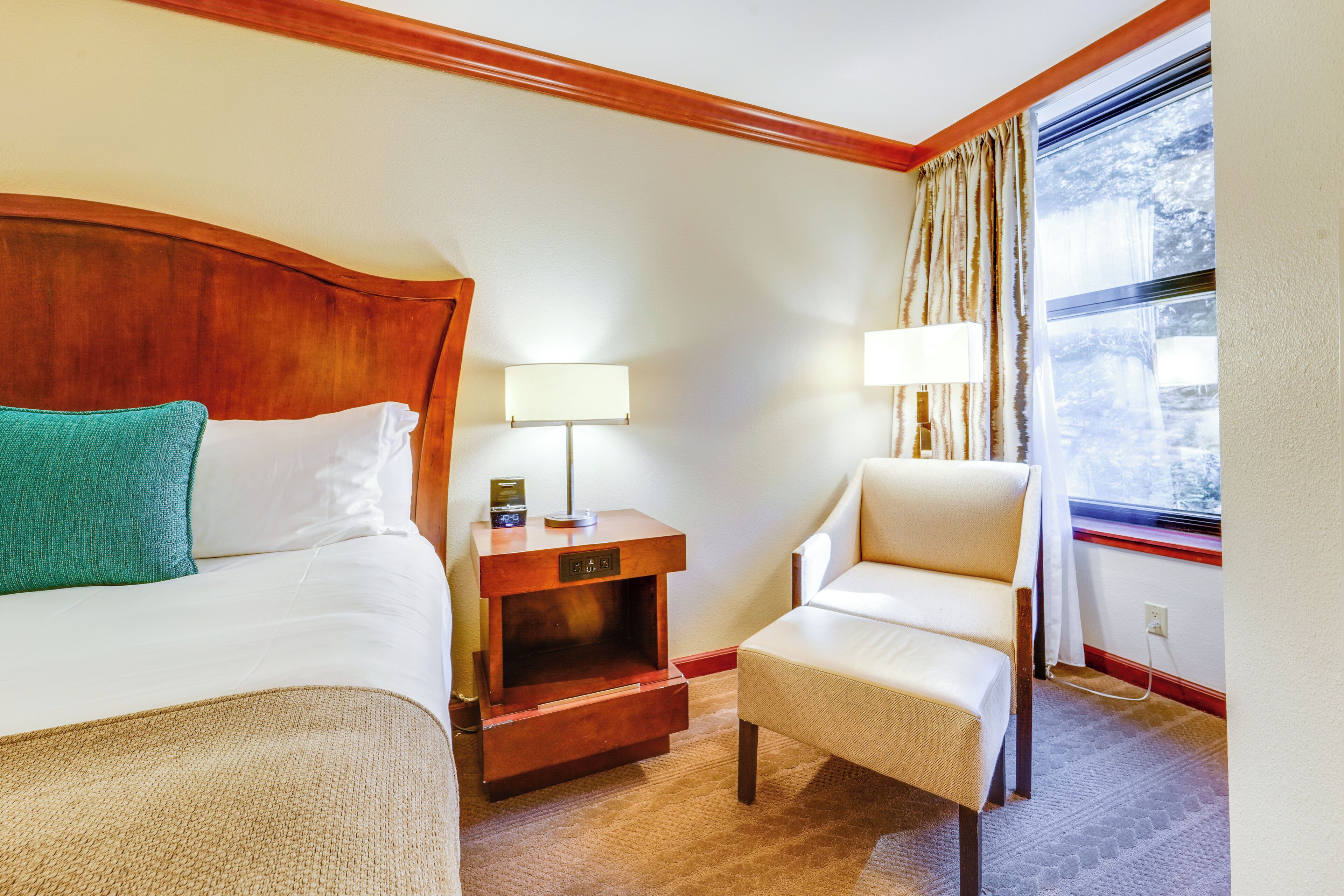 A hotel room with a bed, a nightstand with a lamp, a chair, and a window with curtains.