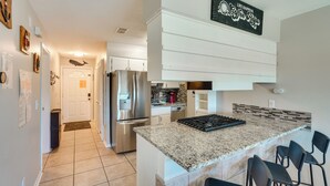 A modern kitchen with a granite countertop, stainless steel appliances, and a bar area with chairs. - Walk to Beach + Restaurants: PCB Resort Condo! (Panama City Beach)