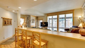 A spacious living area with a wooden bar, seating, and a large window offering a view. - 1/2 Mi to Granby Ranch: Townhome w/ Fireplace! (Granby)