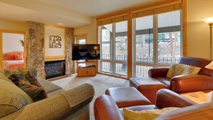 A cozy living room with a stone fireplace, leather sofas, and large windows offering a view of the outdoors. - 1/2 Mi to Granby Ranch: Townhome w/ Fireplace! (Granby)